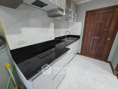 Modern kitchen with sleek black countertops and white cabinetry, featuring a built-in sink and electric stove.