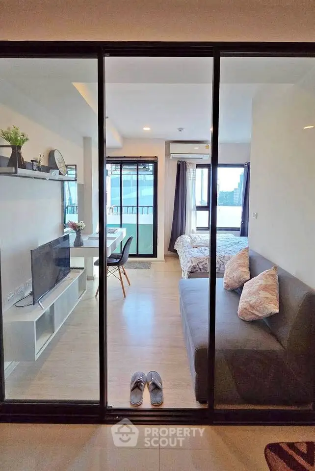 Modern studio apartment with open layout, featuring a cozy living area and bedroom separated by glass doors.