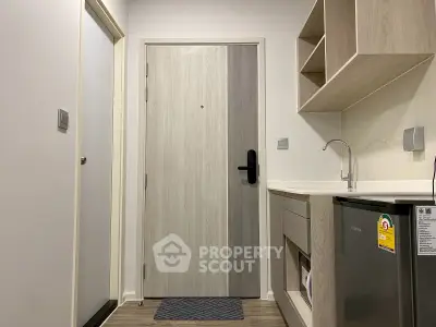 Modern apartment entrance with sleek kitchen area and wooden cabinetry