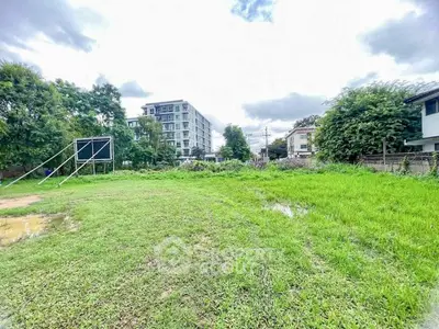 Spacious green land plot with potential for development, surrounded by lush greenery and modern buildings.
