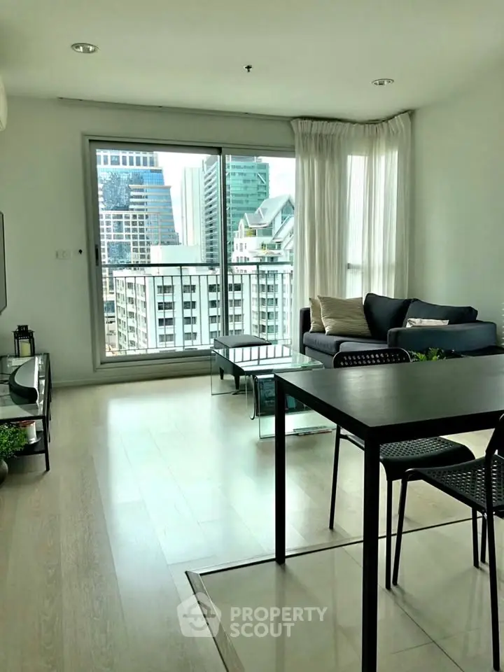 Modern living room with city view, sleek furniture, and natural light in a high-rise apartment.