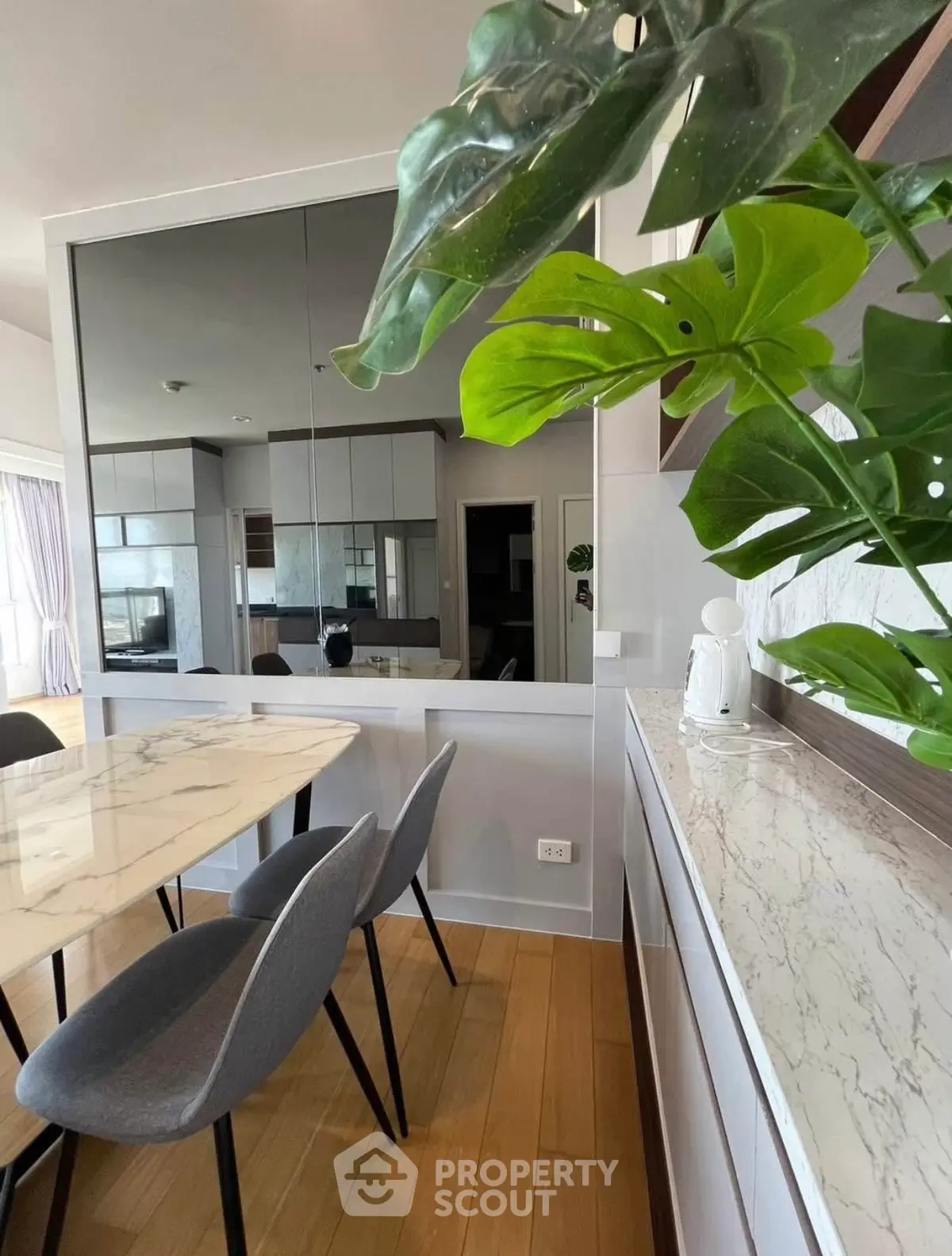 Modern dining area with marble table and stylish chairs, featuring a large mirror and lush green plant.