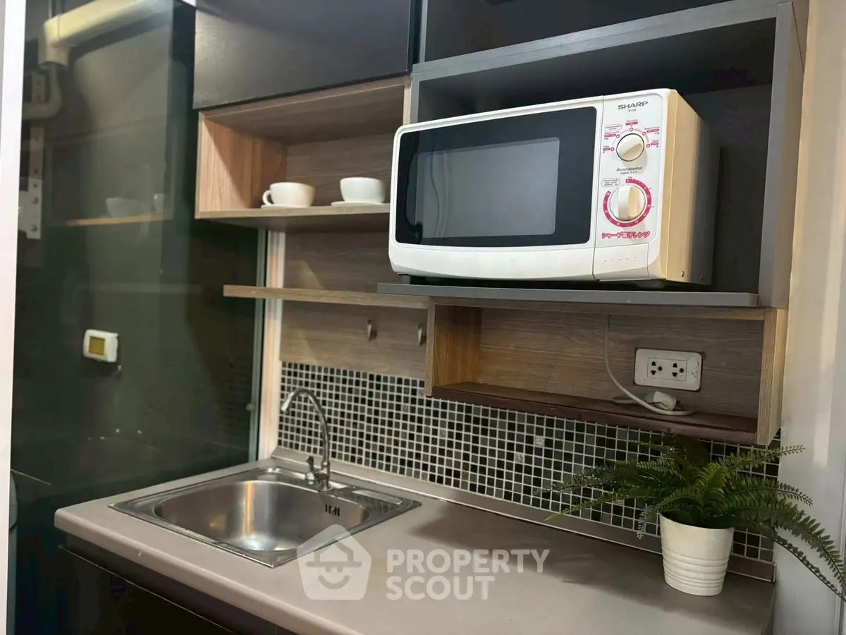 Modern kitchen with microwave and sink, featuring sleek cabinetry and stylish backsplash.