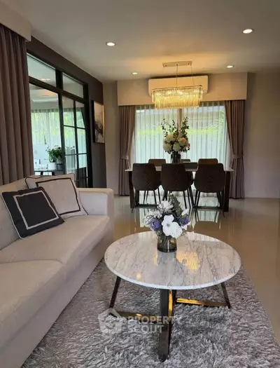 Elegant living room with modern decor and dining area, featuring a chic chandelier and plush furnishings.