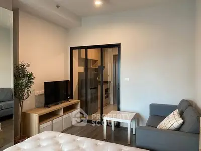 Modern living room with sliding glass doors leading to a sleek kitchen, featuring cozy seating and a flat-screen TV.