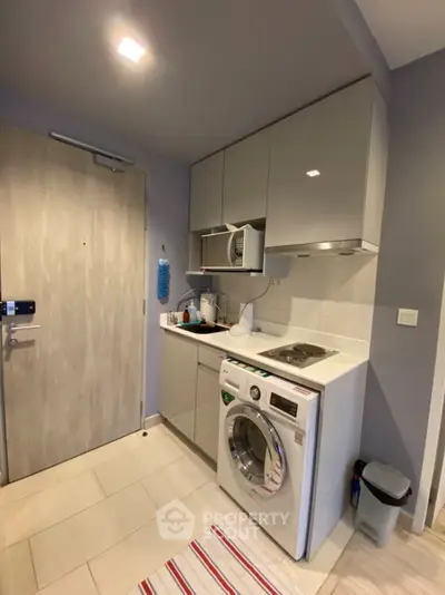 Compact modern kitchen with washing machine and sleek cabinetry in cozy apartment.