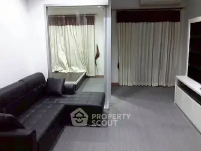 Spacious living room with modern black leather sofa and large windows with curtains.