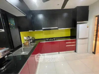 Modern kitchen with sleek red cabinets and black countertops, featuring a gas stove and stainless steel fridge.