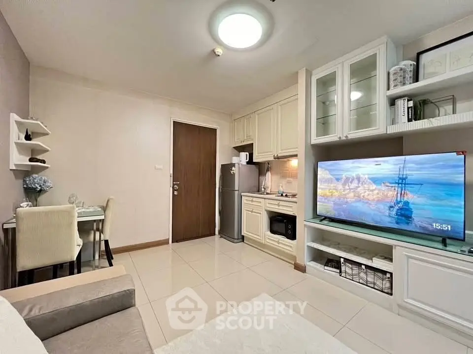 Cozy living room with modern kitchen and dining area, featuring elegant decor and a flat-screen TV.