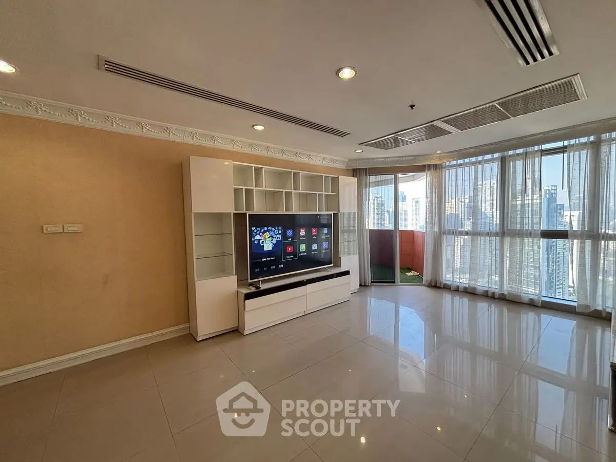 Spacious living room with modern TV unit and city view through large windows.