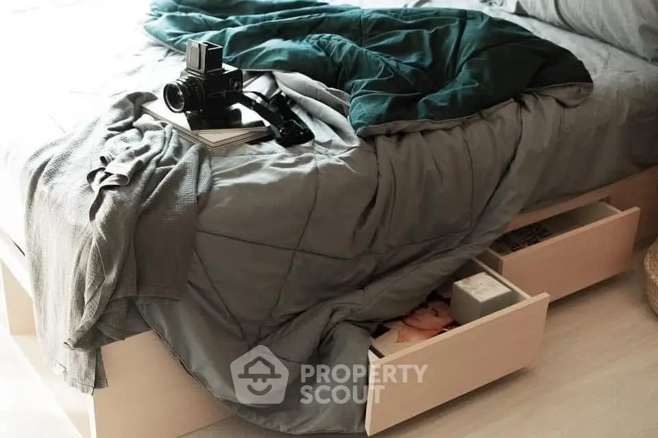 Cozy bedroom with stylish bedding and camera on bed, featuring under-bed storage drawers.