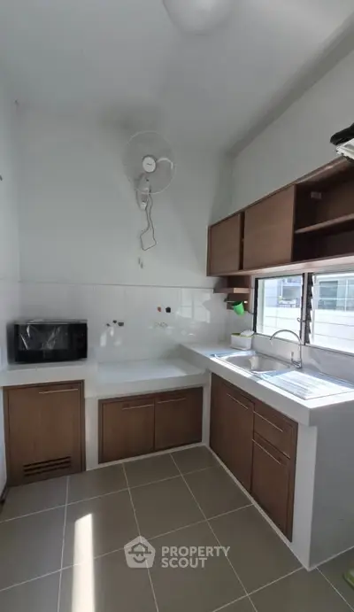 Modern kitchen with sleek cabinetry and ample natural light, featuring a microwave and wall-mounted fan.