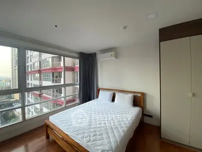 Spacious bedroom with large windows offering city views in modern apartment.