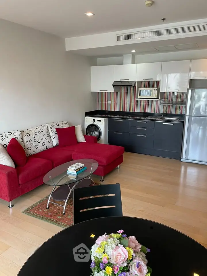 Modern open-plan living room with stylish kitchen and vibrant red sofa, featuring a washing machine and sleek appliances.