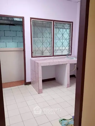 Simple kitchen with tiled countertop and barred windows in a modest home.