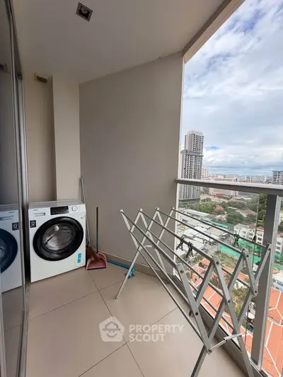 High-rise balcony with washing machine and drying rack overlooking cityscape.
