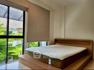 Bright bedroom with large window and modern bed frame, offering a serene view of lush greenery.