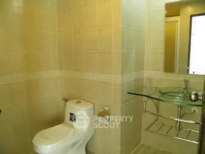 Modern bathroom with glass sink and tiled walls, featuring a sleek toilet design.