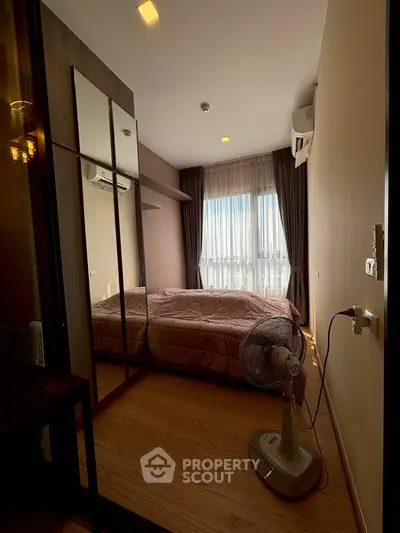 Cozy bedroom with wooden flooring, mirrored wardrobe, and large window with curtains.
