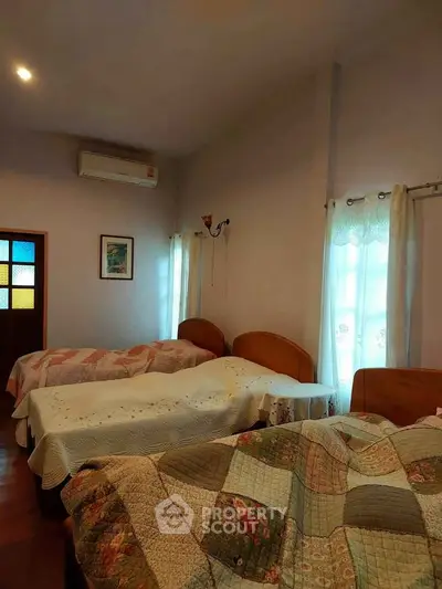 Cozy bedroom with three beds and natural light, perfect for family or group stays.