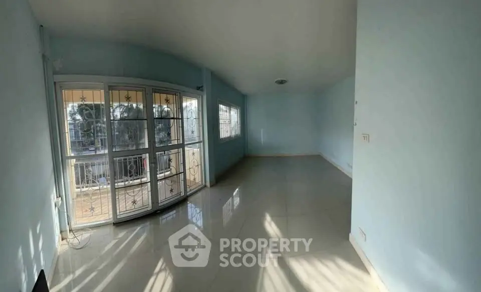 Spacious sunlit living room with large windows and glossy tiled floors.