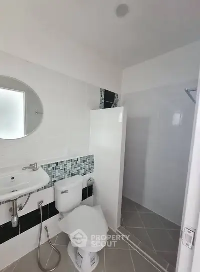 Modern bathroom with sleek design and tiled accents, featuring a shower and round mirror.