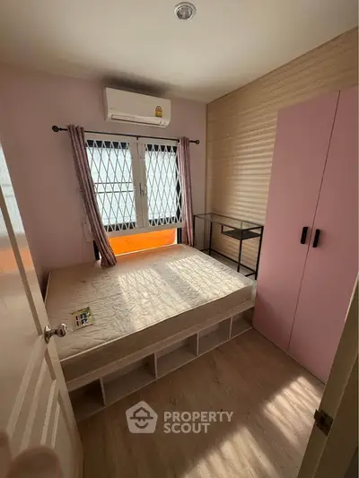 Cozy bedroom with pink accents, featuring a bed, wardrobe, and air conditioning, perfect for a comfortable living space.