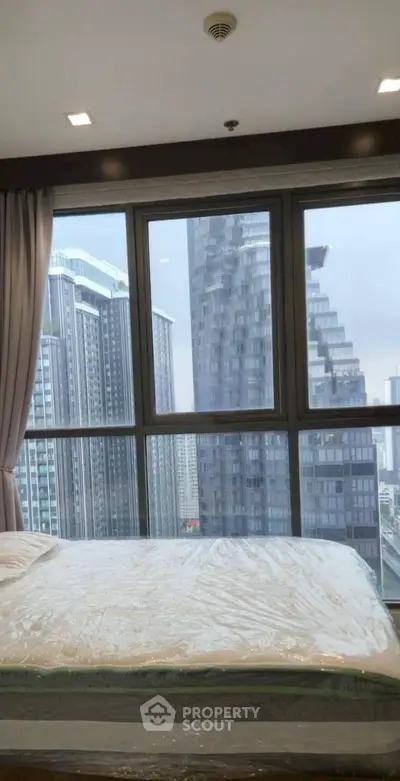 Modern bedroom with large windows offering stunning cityscape views in a high-rise apartment.