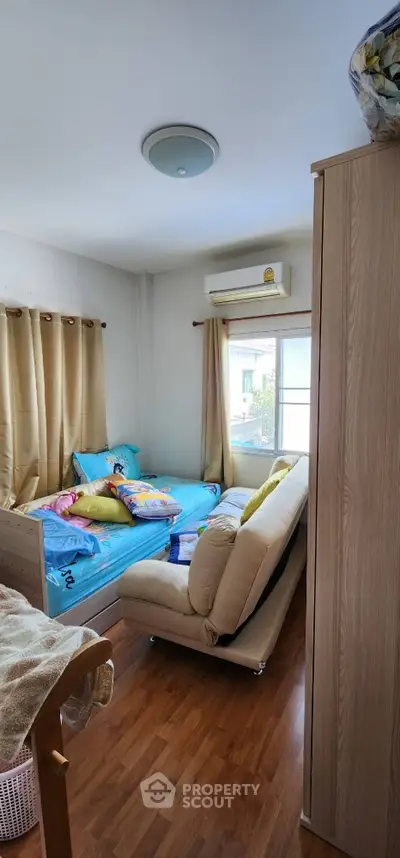 Cozy bedroom with wooden flooring and natural light, featuring a comfortable bed and sofa.