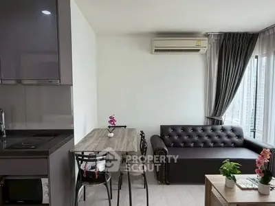 Modern living room with sleek furniture and natural light, featuring a compact kitchen area.