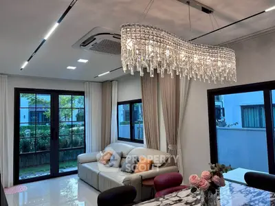 Luxurious living room with elegant chandelier and modern decor, featuring large windows and a cozy sofa.