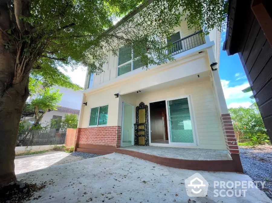 Charming two-story home with a spacious front patio and balcony, nestled under the shade of mature trees in a serene neighborhood.