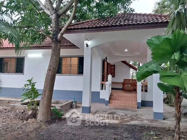 Charming single-story home with tiled roof and inviting front porch surrounded by lush greenery.