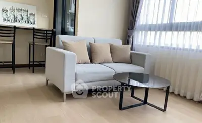 Modern living room with stylish sofa and glass coffee table, featuring large windows for natural light.