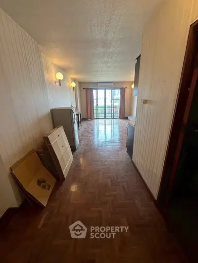 Spacious hallway leading to a bright living area with parquet flooring and balcony view.