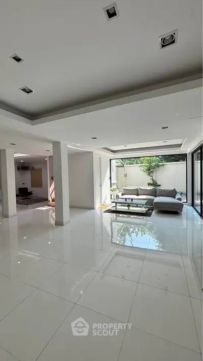 Spacious modern living room with sleek white tiles and large windows offering natural light.
