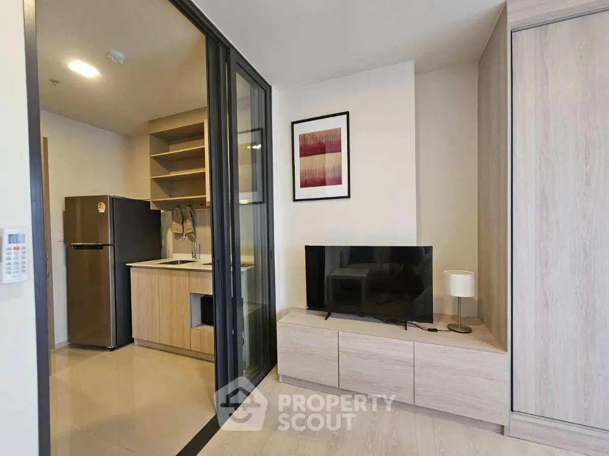 Modern apartment interior with sleek kitchen and cozy living area featuring a TV and stylish decor.