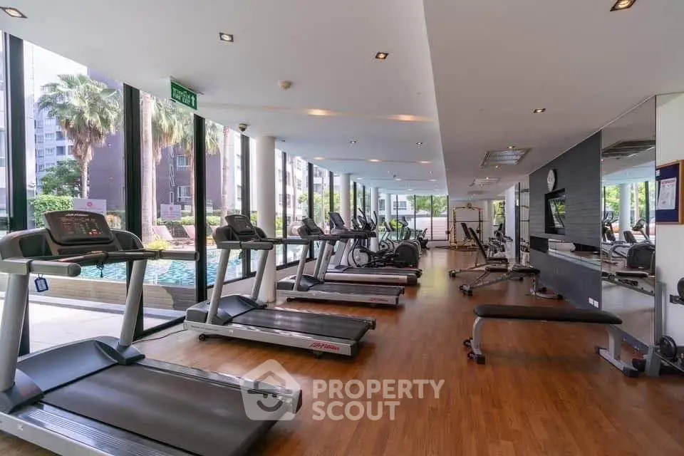 Spacious gym with modern equipment and pool view in luxury residential building.
