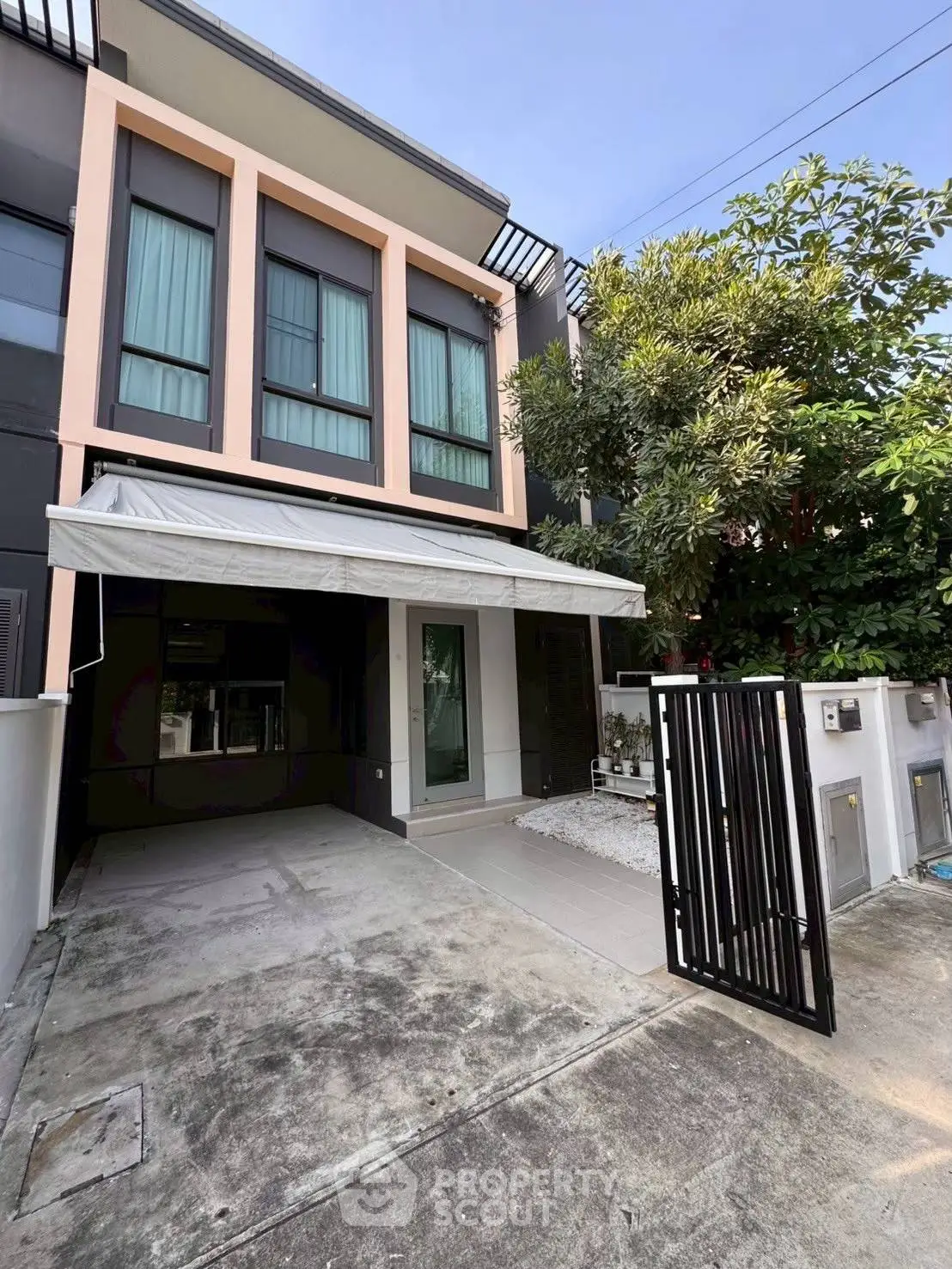 Modern townhouse exterior with gated entrance and driveway, featuring sleek design and lush greenery.