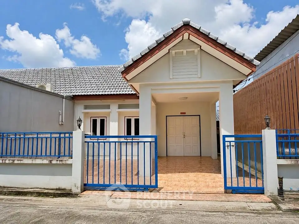 Charming single-story house with blue fence and tiled porch under a clear sky.