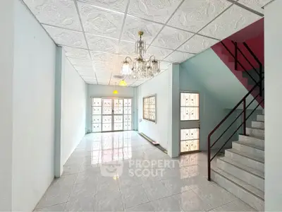Spacious interior with elegant chandelier and tiled flooring, featuring a staircase and large windows for natural light.