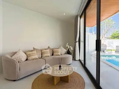 Modern living room with pool view, featuring a cozy sofa and large glass doors opening to outdoor space.