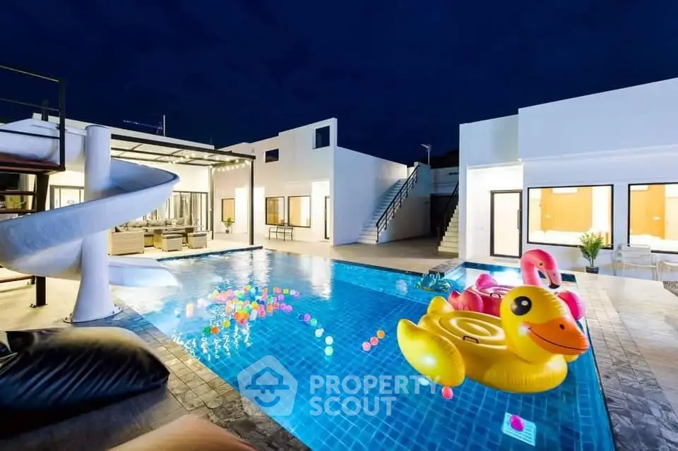 Luxurious modern villa with illuminated pool and playful inflatables, perfect for entertaining and relaxation.