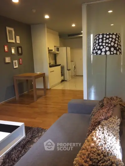 Modern living room with cozy sofa, stylish lamp, and compact kitchen area featuring washing machine.