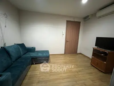 Cozy living room with teal sofa and wooden flooring, featuring a TV stand and air conditioning.