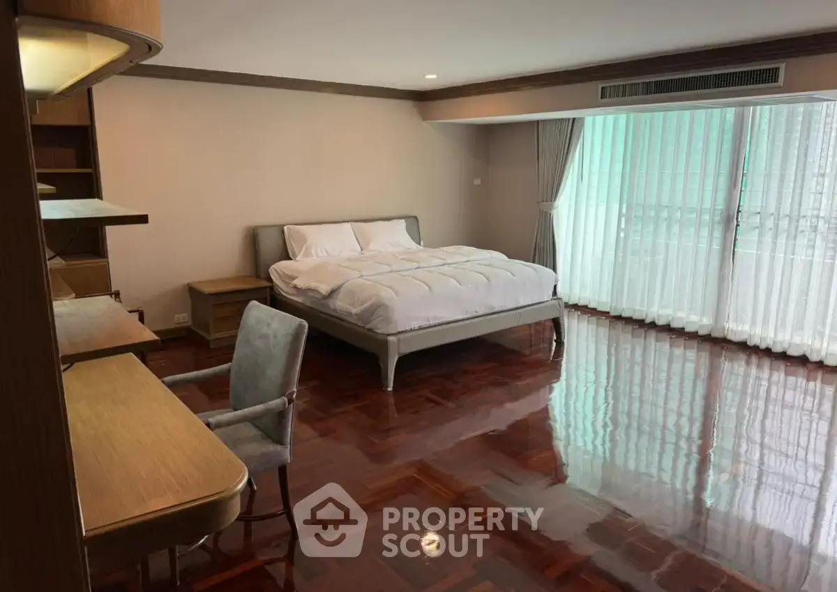 Spacious bedroom with polished wooden floors and large window for natural light.