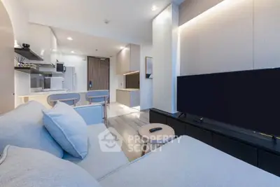 Modern living room with sleek design and open kitchen layout, featuring a cozy sofa and large flat-screen TV.