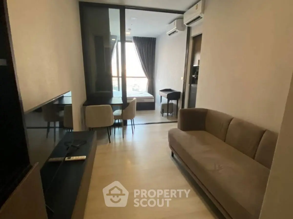 Modern living room with sleek furniture and dining area, featuring large windows for natural light.