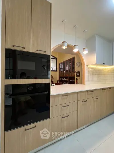 Modern kitchen with sleek cabinetry and built-in oven, featuring elegant pendant lighting and open archway design.