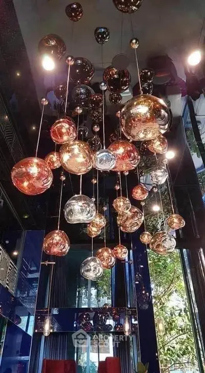 Stunning modern chandelier in luxurious interior with glass walls and lush greenery view.